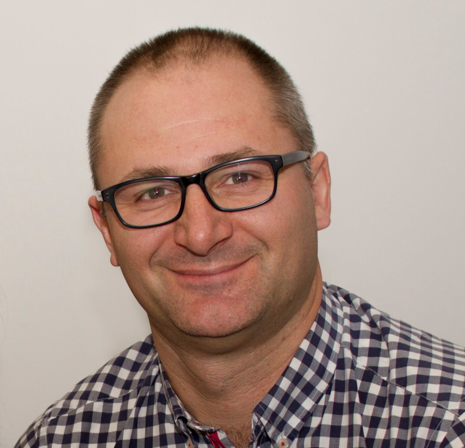 A man wearing glasses and a plaid shirt smiles for the camera