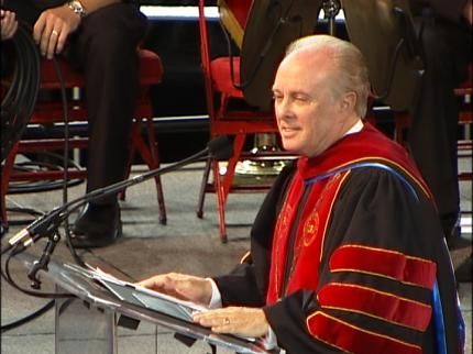 Dr. Mark Rutland in a graduation gown is sitting at a podium