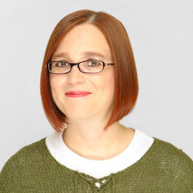 A woman with red hair wearing glasses and a green sweater