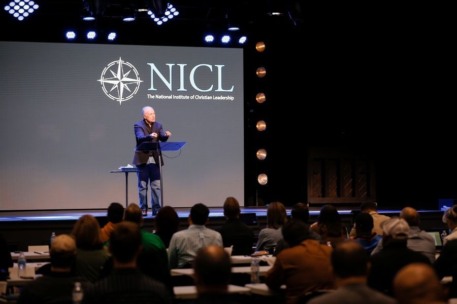 A man is giving a speech in front of a screen that says nicl