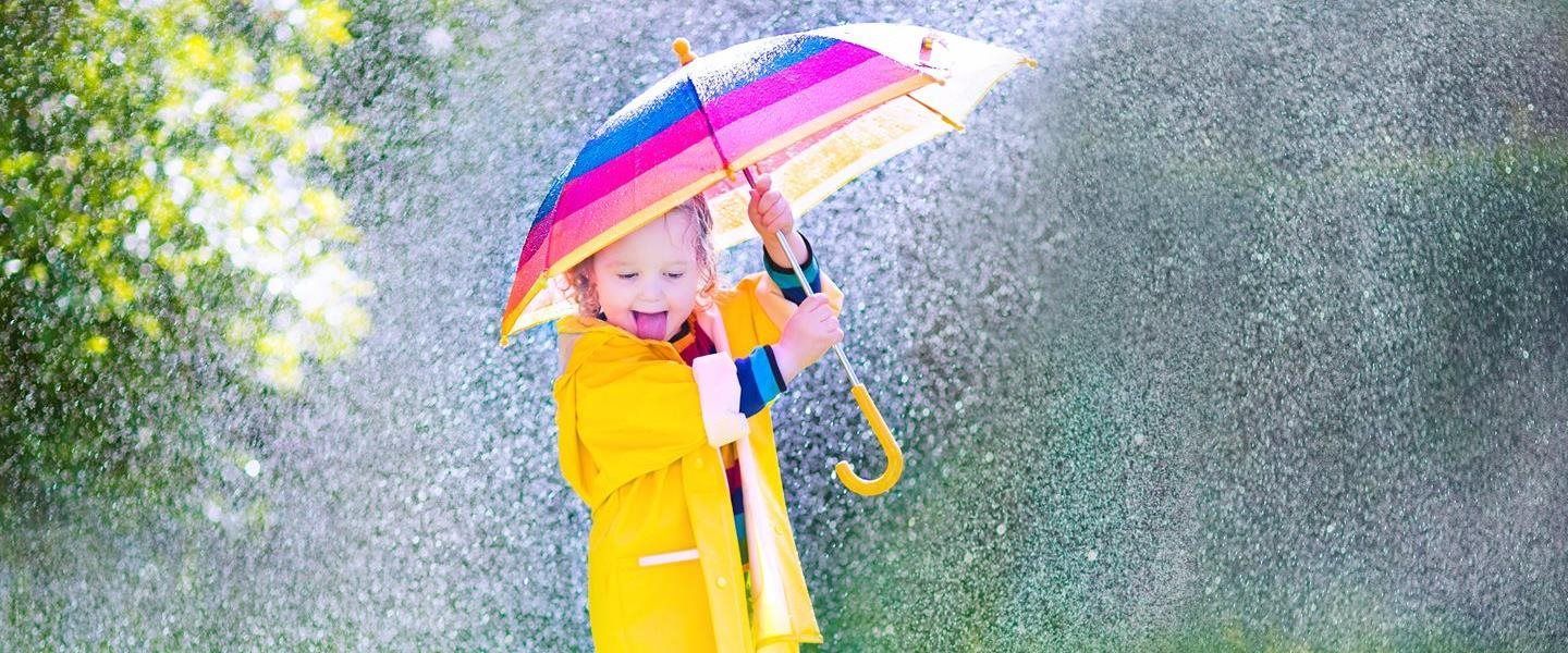 Child in yellow raincoat holding a colorful umbrella in the rain