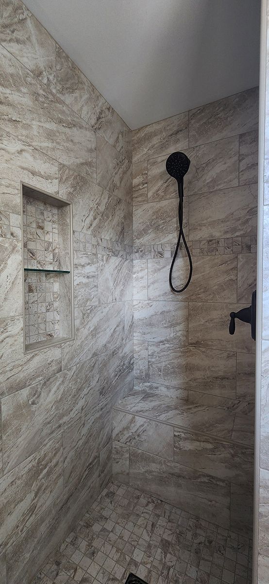 A walk in shower with a shower head and a shelf.