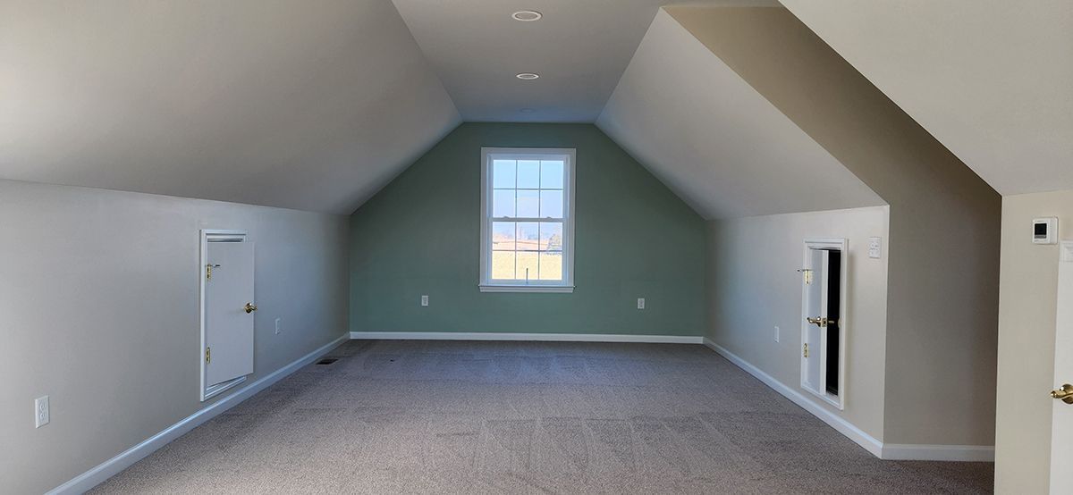 An empty attic with a vaulted ceiling, a window and two storage areas