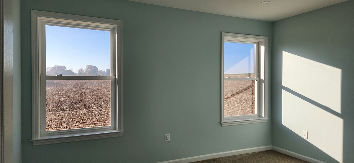 A room with two windows and a field in the background.