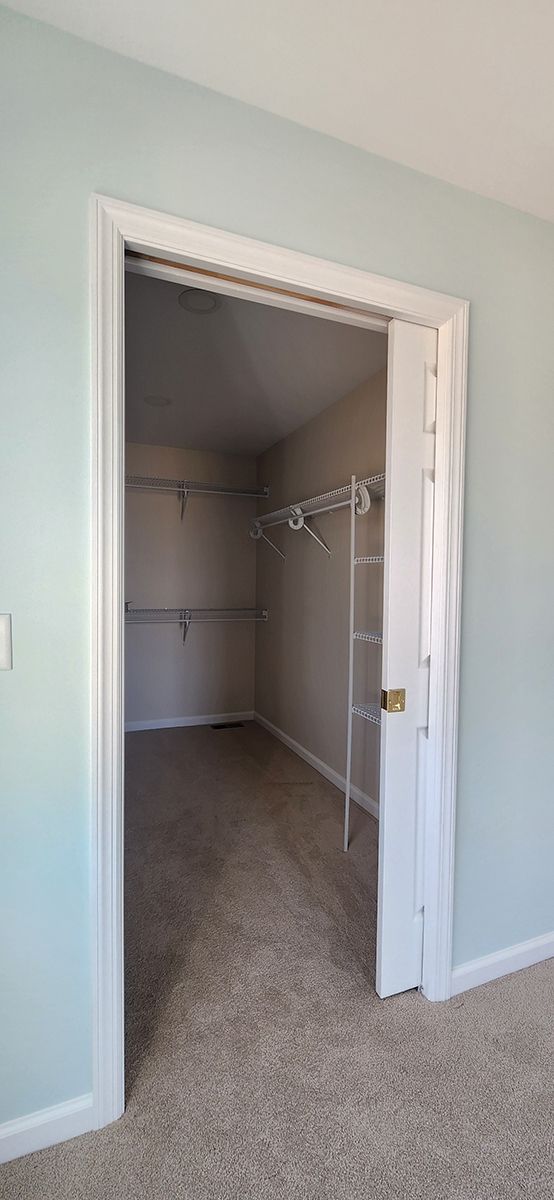 A walk in closet with a carpeted floor, white door and shelving