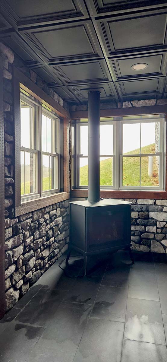 wood stove in corner of room with windows and stone wall