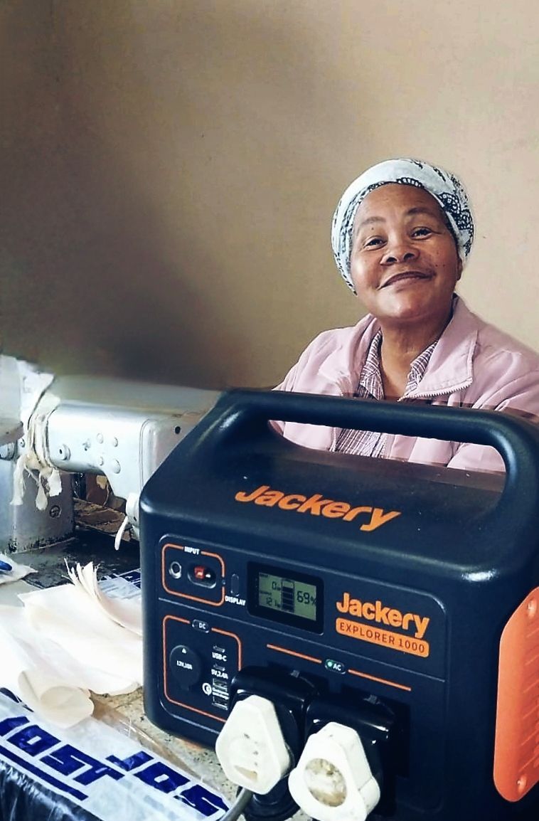 Photo of a female seamstress in South Africa with a new power pack to help her work during a time of loadshedding.