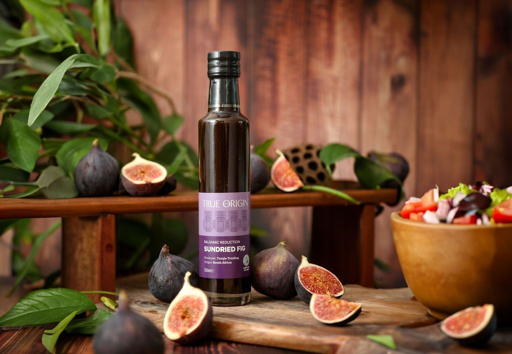 A tall bottle of purple Sundried Fig Balsamic Reduction surrounded by chopped figs.