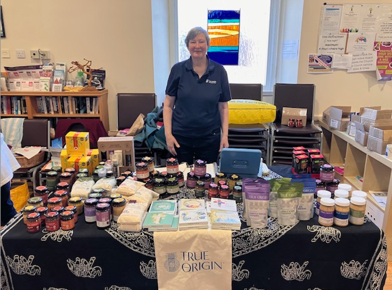 A woman standing at church fair trade stall with lots of delicious fair trade products available