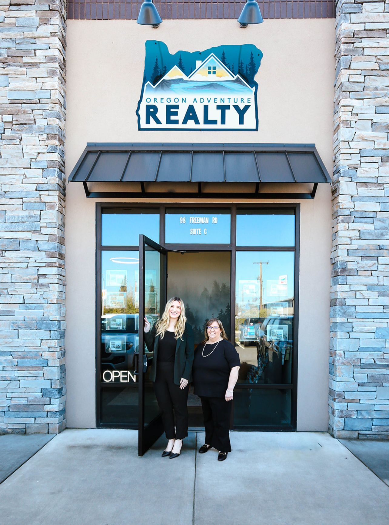 Two women are standing in front of a real estate office.