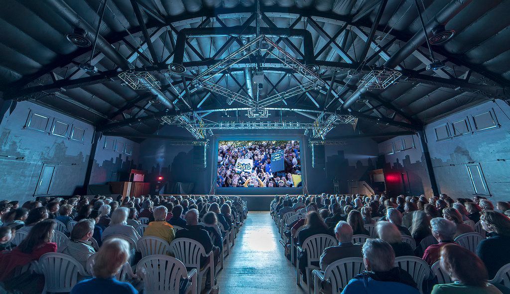 A large group of people are sitting in chairs in front of a large screen.