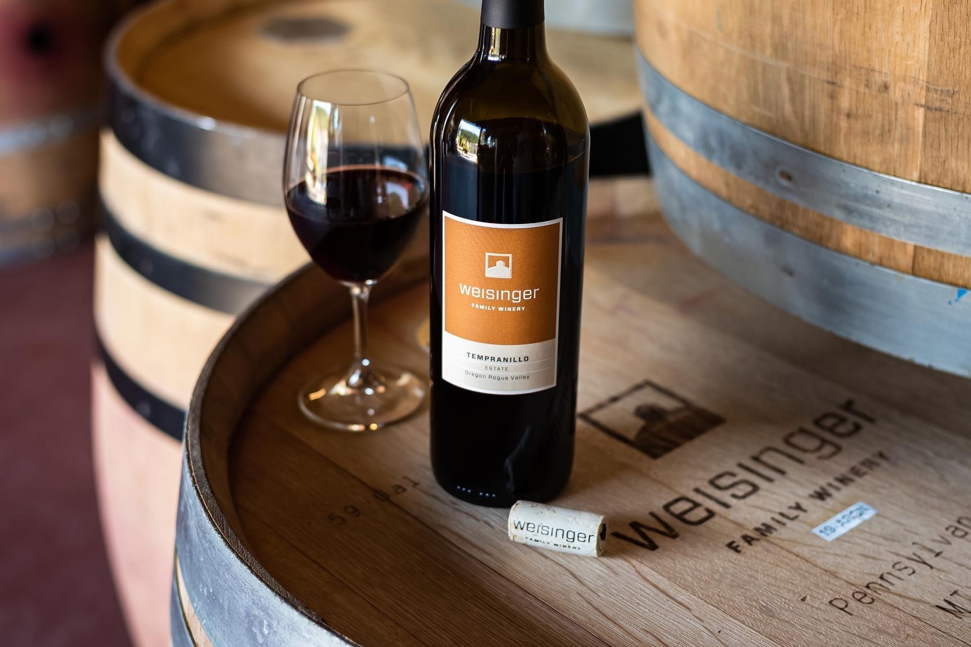 A bottle of wine is sitting on top of a wooden barrel next to a glass of wine.