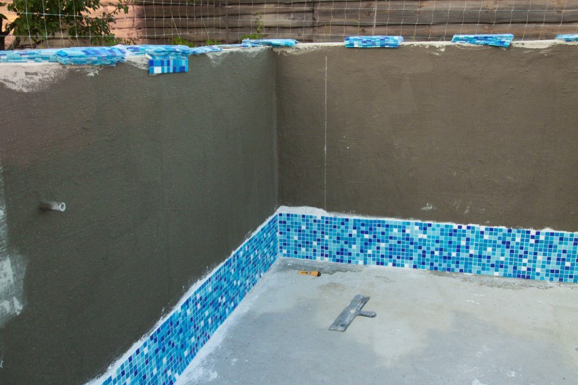 Empty pool with gray walls and blue mosaic tile trim, covered with a tarp or plastic liner.