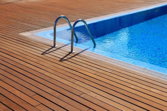 Pool ladder beside blue swimming pool on a wooden deck