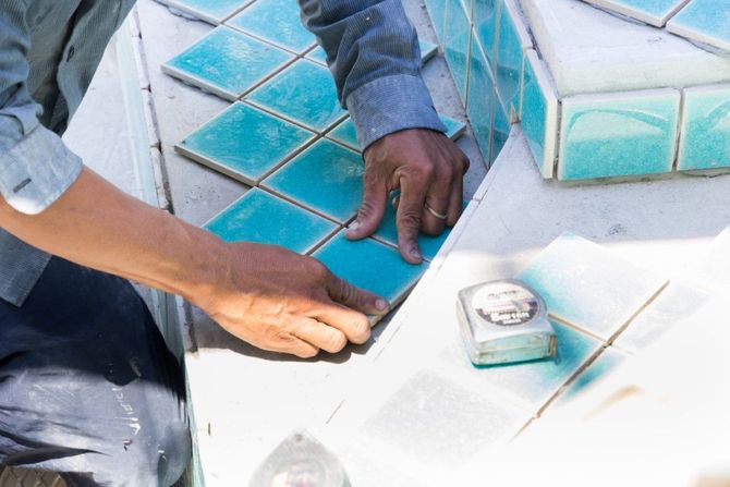 Two hands laying blue mosaic tiles on a curved white surface
