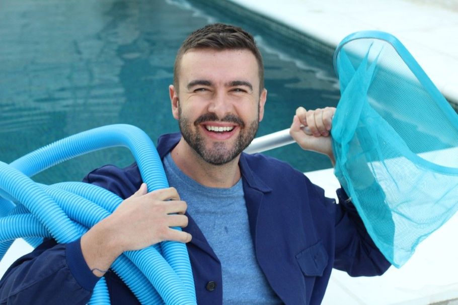 Smiling man in a pool holding blue swim noodles and a net