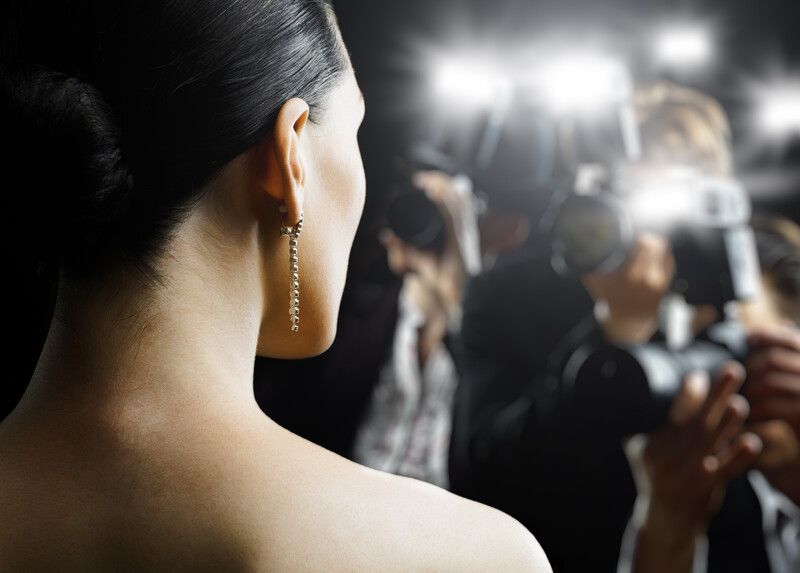 A woman wearing earrings is being photographed by a man with a camera.