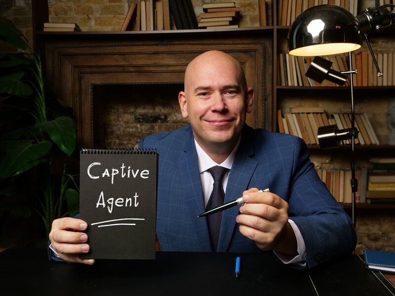 A man in a suit and tie is holding a notebook that says captive agent.