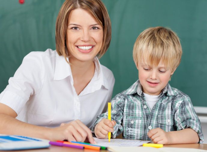 A teacher is helping a young boy with his homework in a classroom.