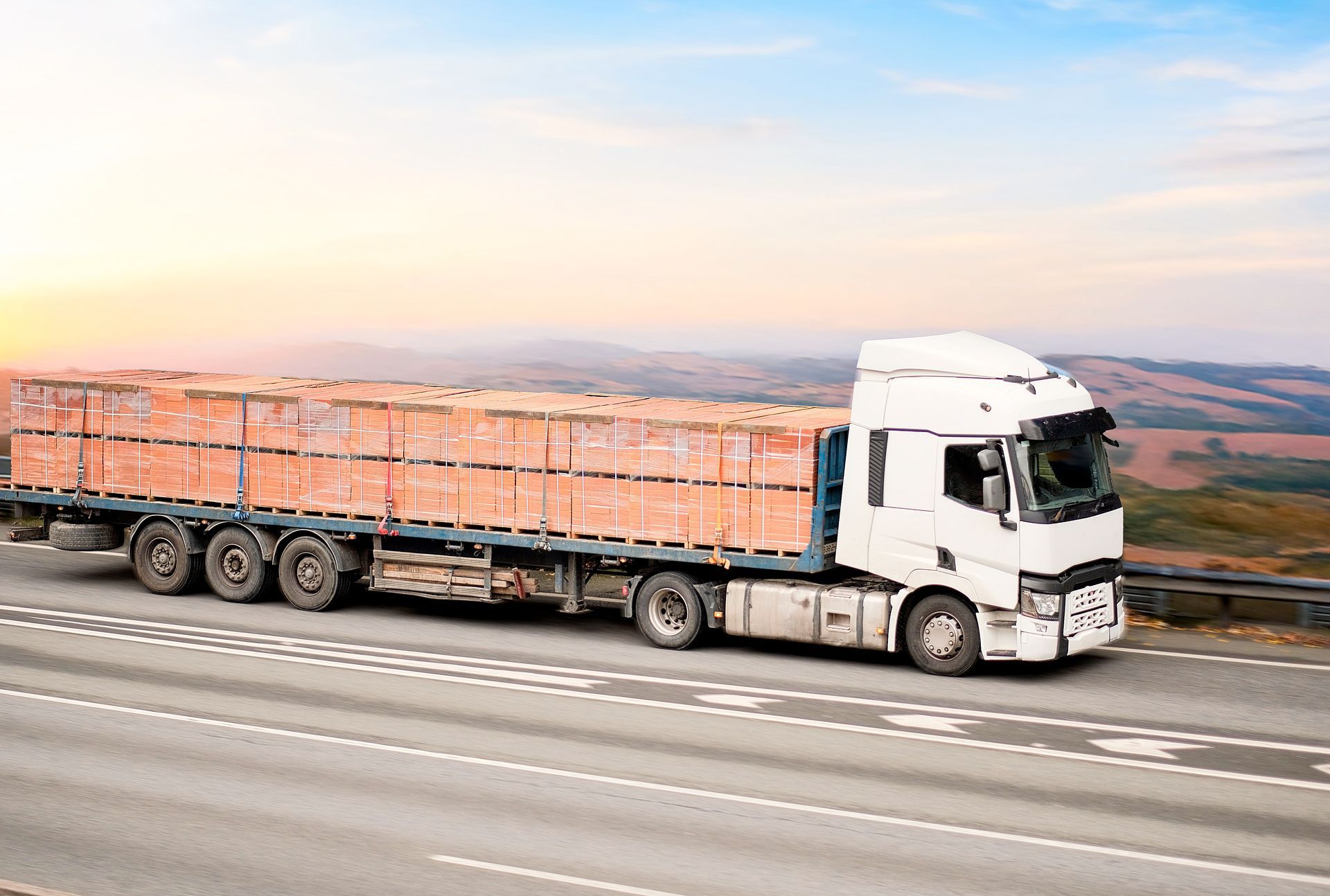 White truck hauling a load of red bricks on a highway with a blue sky background.