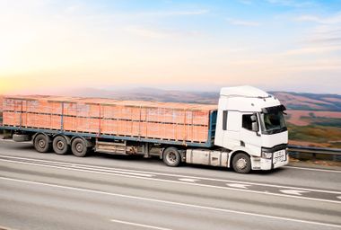 White truck hauling a load of red bricks on a highway with a blue sky background. White truck hauling a load of red bricks on a highway with a blue sky background.
