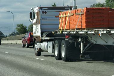 Semi-truck on highway, transporting lumber secured with straps, red car in background. Semi-truck on highway, transporting lumber secured with straps, red car in background.