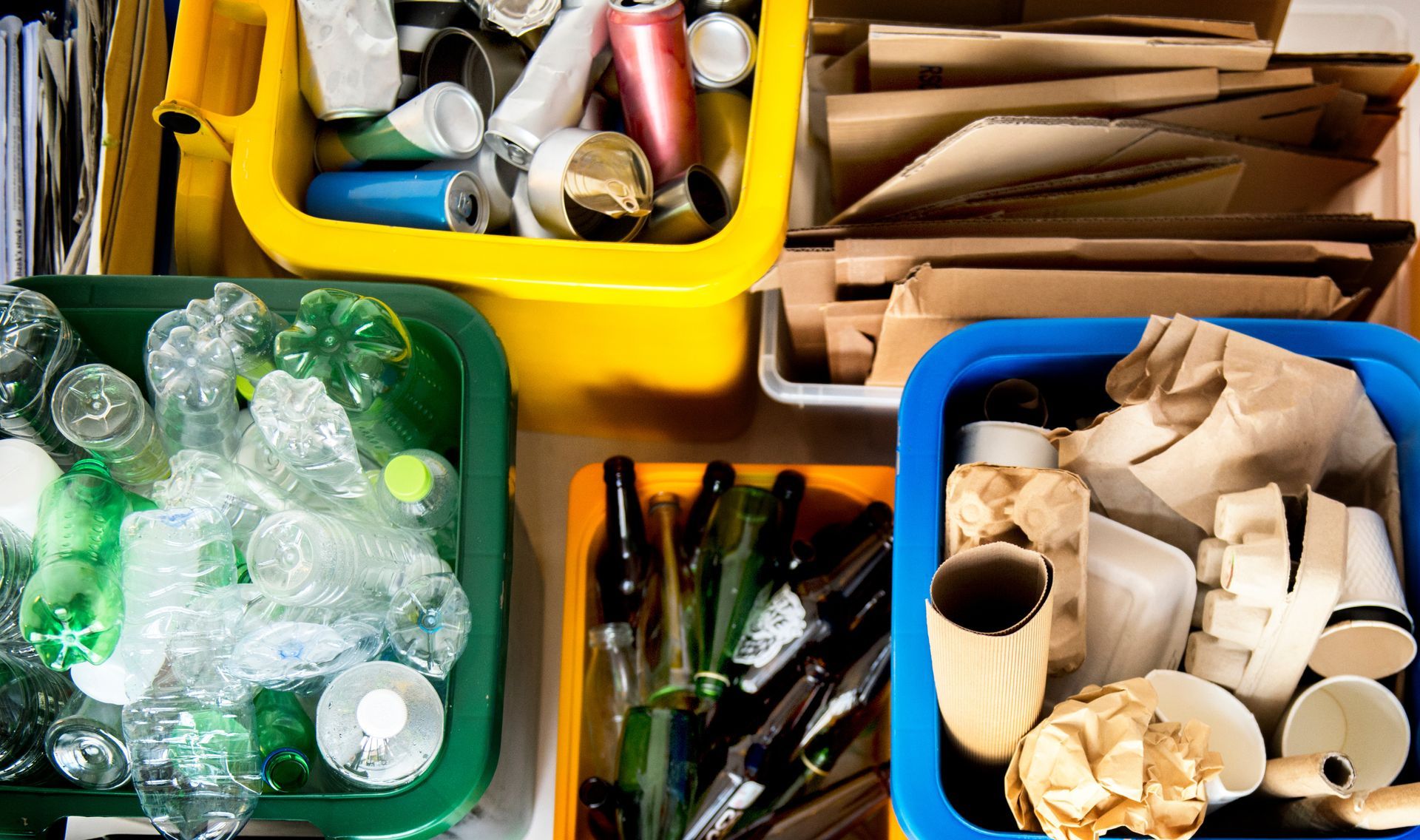Recycling bins, sorted by material: plastics in green, metals in yellow, paper in white, and mixed paper in blue.