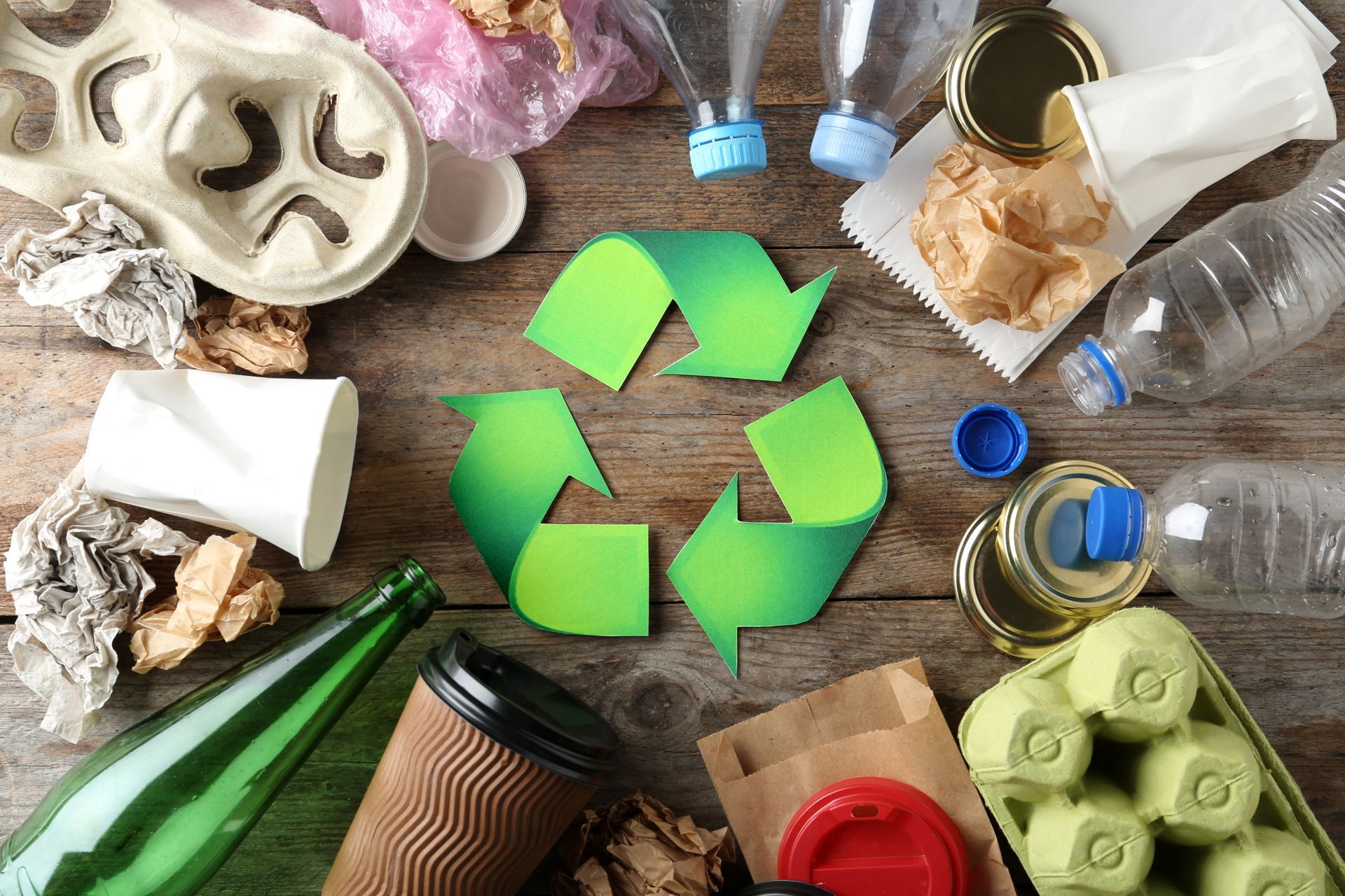 Recycling symbol surrounded by various recyclable items including glass, plastic, and paper.