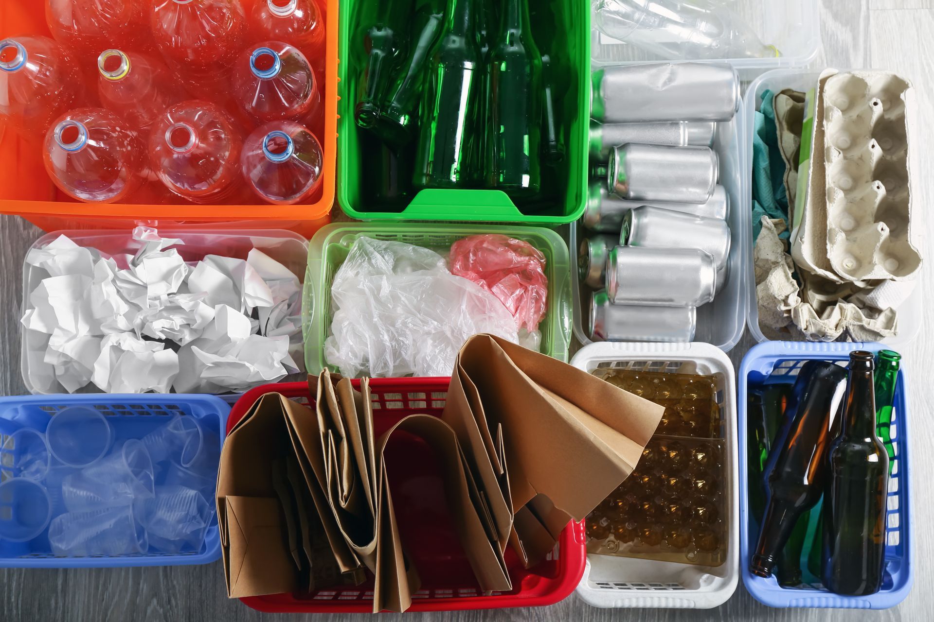 Overhead view of various recycling bins with sorted items: plastic bottles, glass, paper, and food containers.