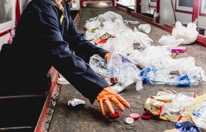 Person sorting plastic waste on a conveyor belt, wearing gloves. Person sorting plastic waste on a conveyor belt, wearing gloves.