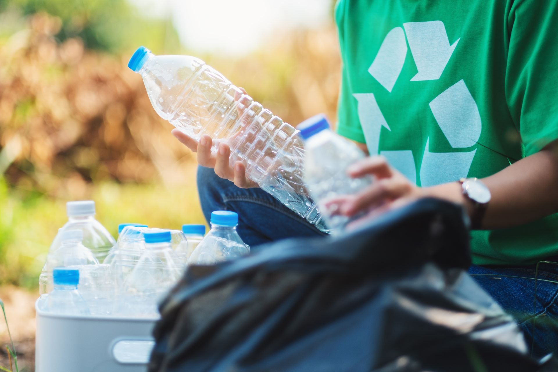 Person in green shirt with recycling symbol collecting plastic water bottles.