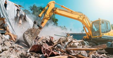 Yellow excavator demolishes a building, kicking up dust and debris. Yellow excavator demolishes a building, kicking up dust and debris.