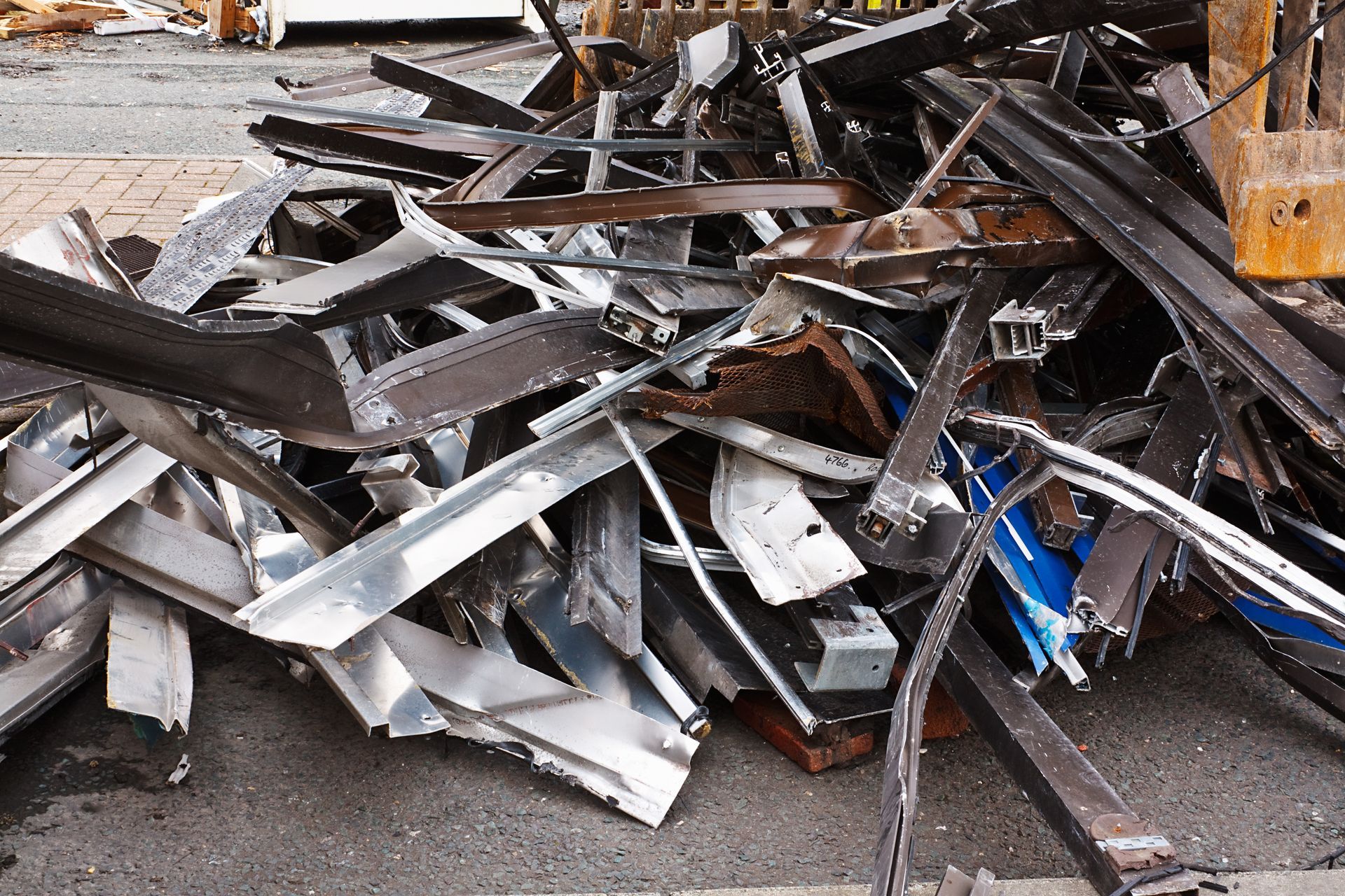 Scrap metal pile on asphalt, containing various metal shapes and pieces; outside.