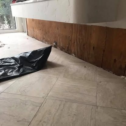 Room with light tile floor, damaged wood paneling, and a black trash bag.