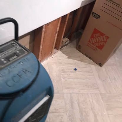 Dehumidifier next to damaged wall. Cardboard box leans against wall. Light-colored floor.