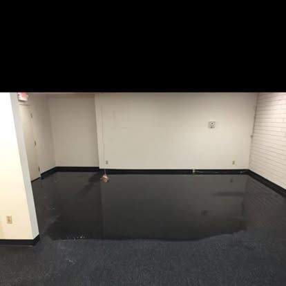 Dark, wet floor in a white-walled room; a single door visible, suggesting a flood.