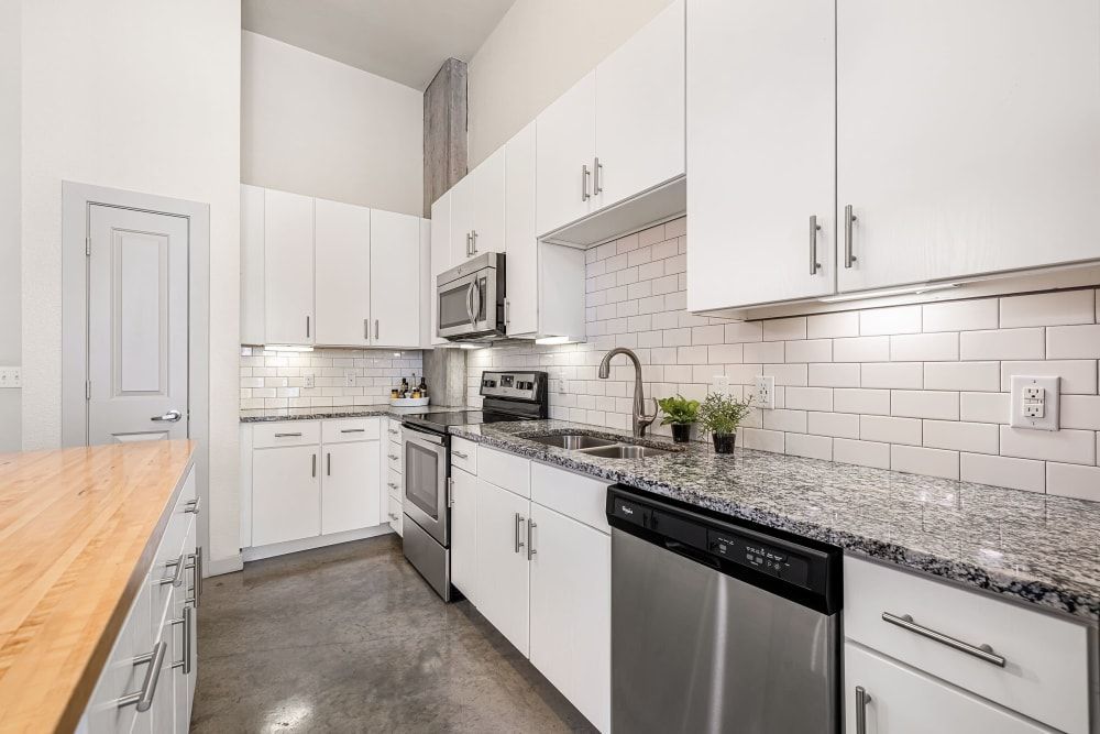 Modern kitchen interior featuring white cabinetry, granite countertops, subway tile backsplash, stainless steel appliances, and a wood butcher block island at Marq on Burnet in Austin, TX.