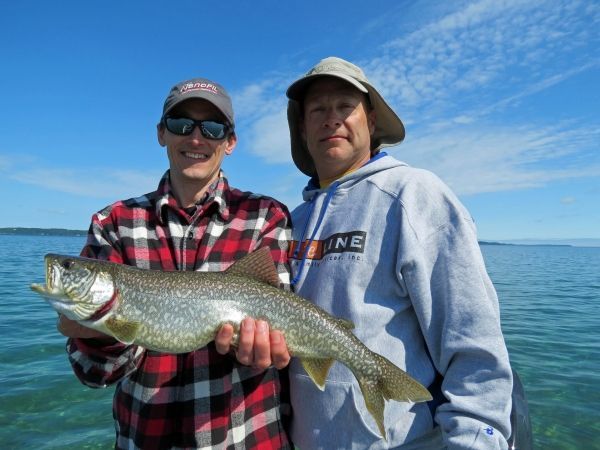 Two men are holding a large fish in front of a body of water.