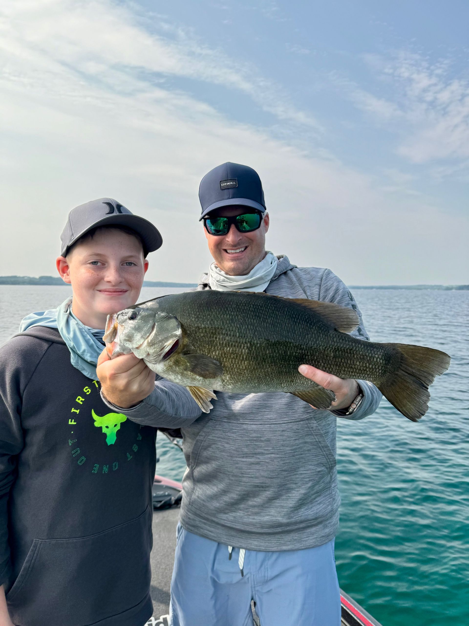 A man and a boy are holding a large bass on a boat.