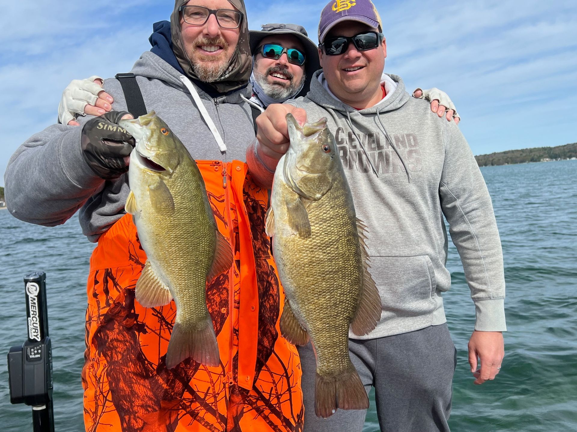 Three men are standing on a boat holding two fish.