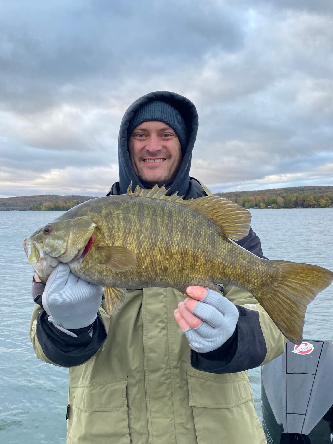 A man is holding a large fish in his hands on a lake.