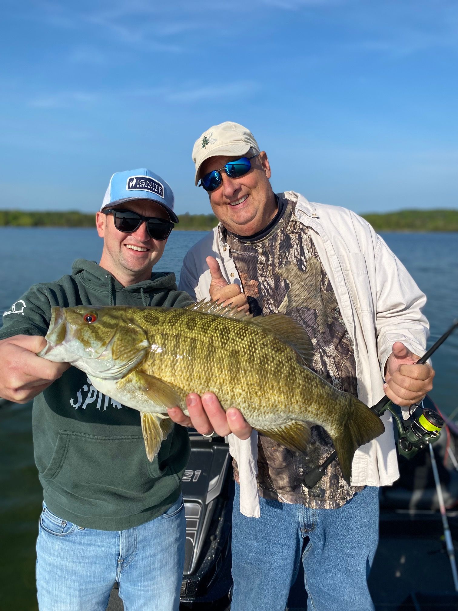 Two men are standing next to each other on a boat holding a large fish.