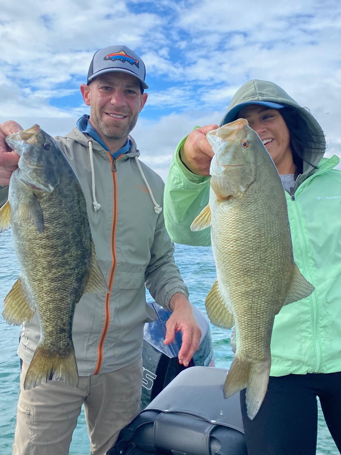 A man and a woman are holding two bass on a boat.