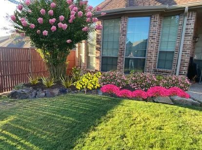 A brick house with a lush green lawn and flowers in front of it.