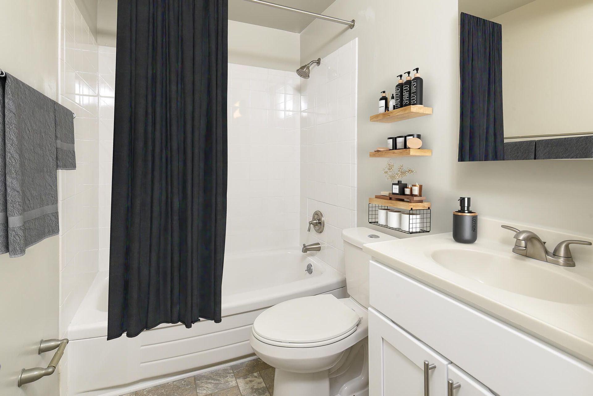 Bathroom with a bathtub/shower, white tiled walls, dark shower curtain, toilet, and white vanity.