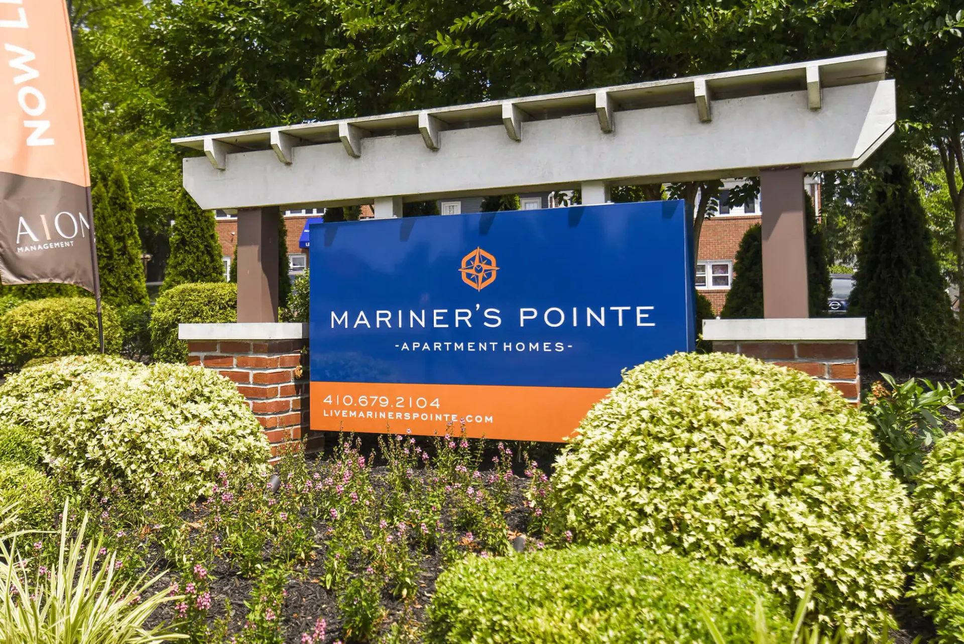 Entrance sign for Mariner's Pointe Apartment Homes with a blue and orange sign and landscaped surroundings.