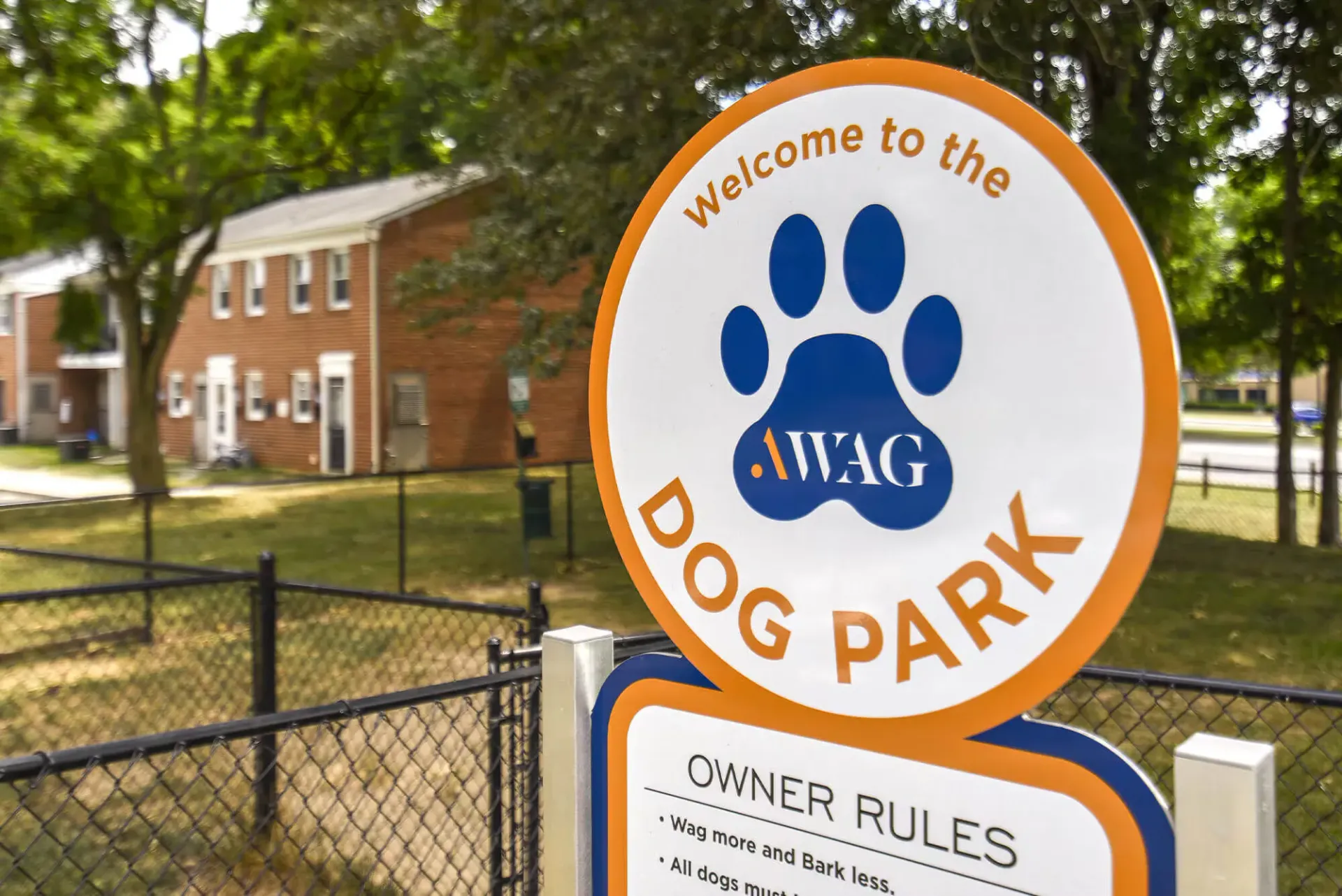 Circular dog park sign with blue paw print and orange border beside a fence.
