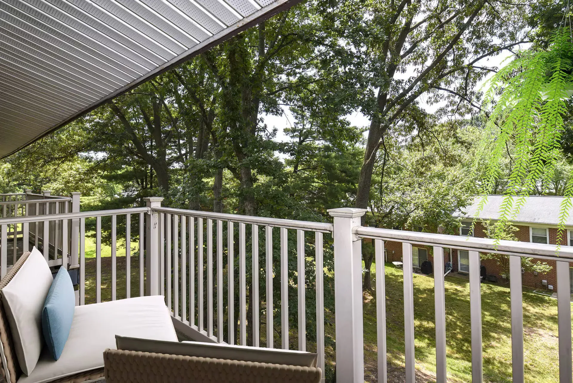 Balcony with white railing and cushioned seating overlooking a leafy courtyard.