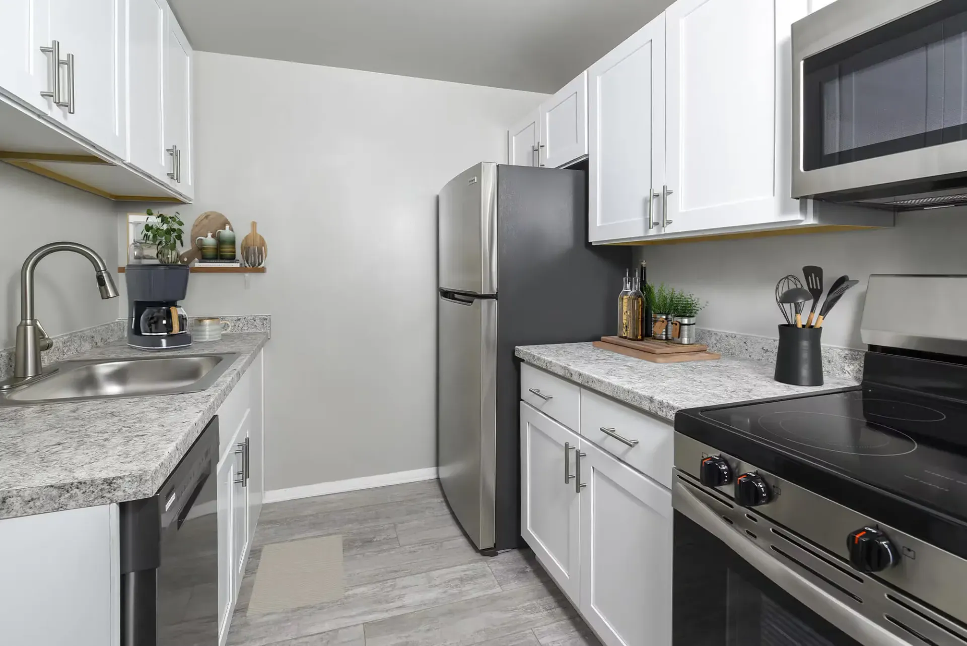 Narrow galley kitchen with white Shaker cabinets, granite countertops, stainless steel refrigerator, stove, microwave, and sink.