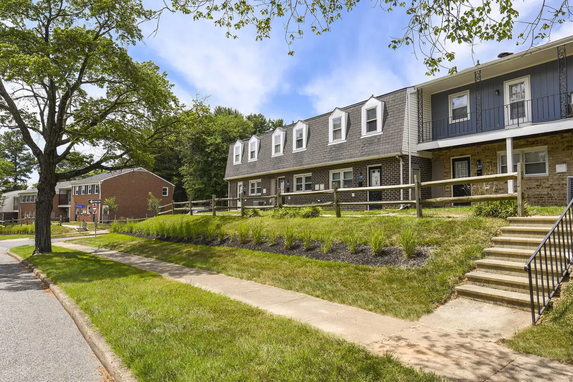 Exterior view of a brick apartment building with lawn, sidewalk, and stairs.